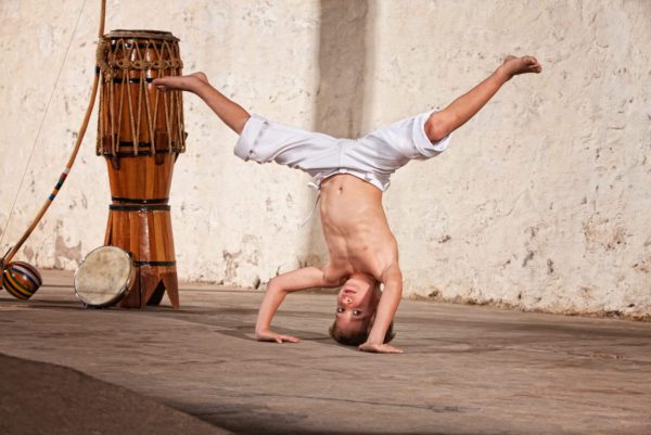 Cute capoeria boy in headstand with African music instruments